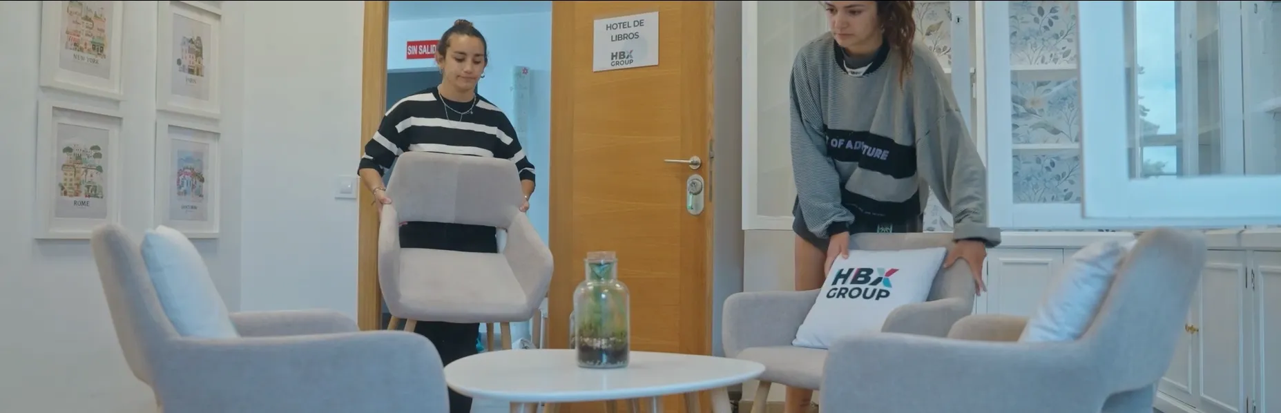 Two people setting chairs with HBX Group pillows into a library room
