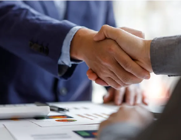 Two people shaking hands formally over a desk full of reports