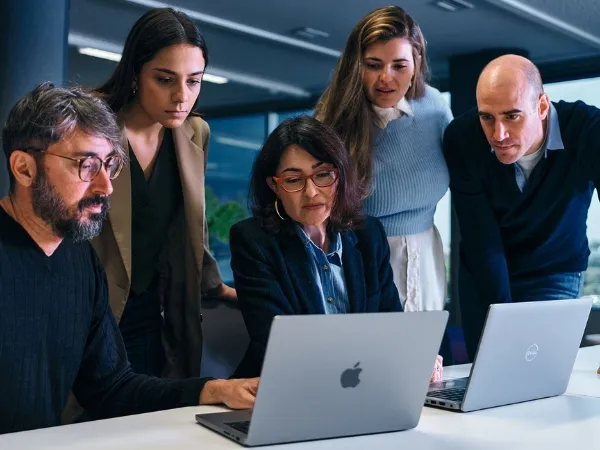 Five pople working together focus on two laptops